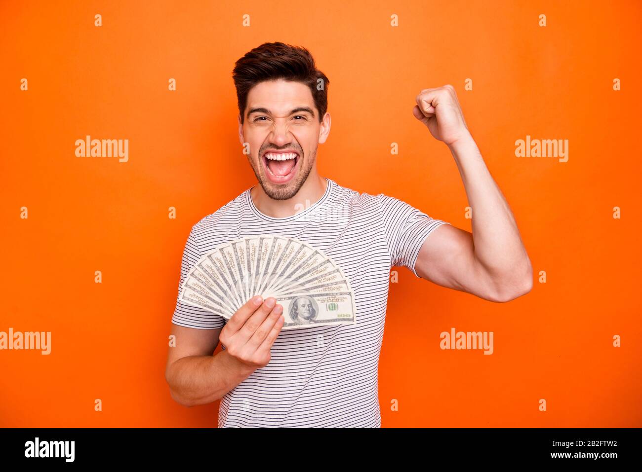 I am rich. Photo of funny attractive guy hold hands fan of bucks first currency salary raise fist screaming wear striped t-shirt isolated bright Stock Photo