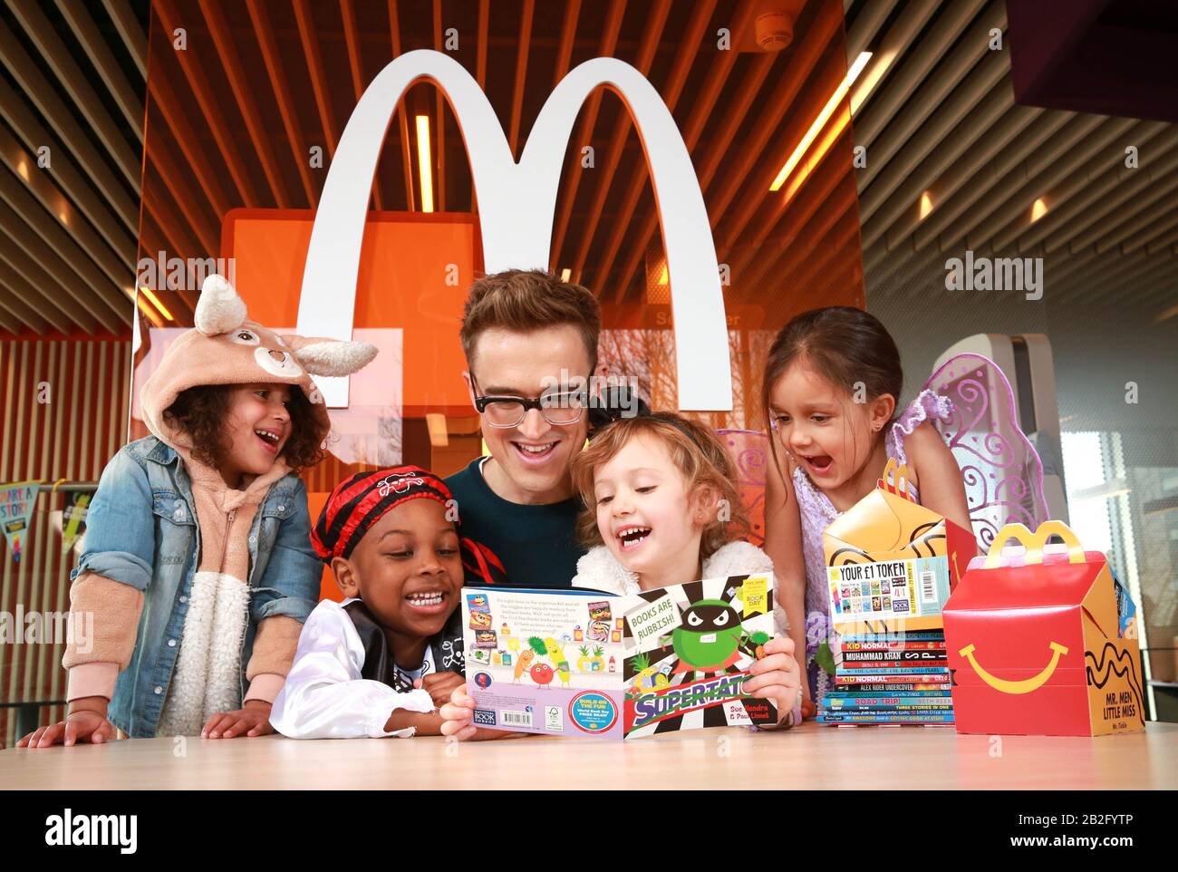 Children's author and musician Tom Fletcher reads to (left to right) four year olds Pearl Prasad, Zane-Ellis Yeboah, Maisie Patey, and five year old Alexandra Ancharaz, as he is unveiled as the new McDonald's Happy Readers Ambassador to celebrate World Book Day, London. PA Photo. Issue date: Tuesday March 3, 2020. Since the beginning of February, the Happy Meal box in the UK and Ireland has included a free book token from World Book Day, giving millions of families' access to one of 12 free books from booksellers across the country through the Happy Readers scheme. Photo cre Stock Photo