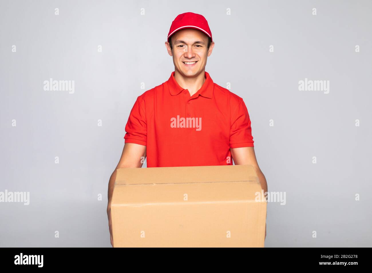Image of a excited happy young delivery man in red cap standing with ...