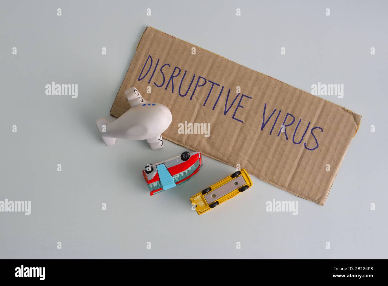 Cardboard sign with message DISRUPTIVE VIRUS, buses and plane model turned upside down. Covid 19 outbreak destroying tourism and world economy Stock Photo
