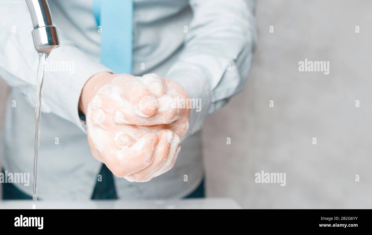 Businessman in blue shirt and tie wash his hands deeply under a faucet with running water. Hand washing is very important to avoid the risk of contagi Stock Photo
