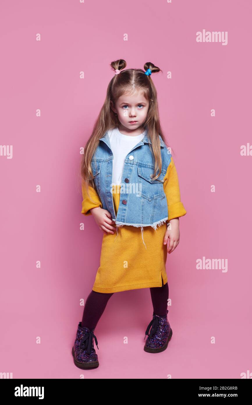 Beautiful stylish little girl in jean clothes posing on pink background