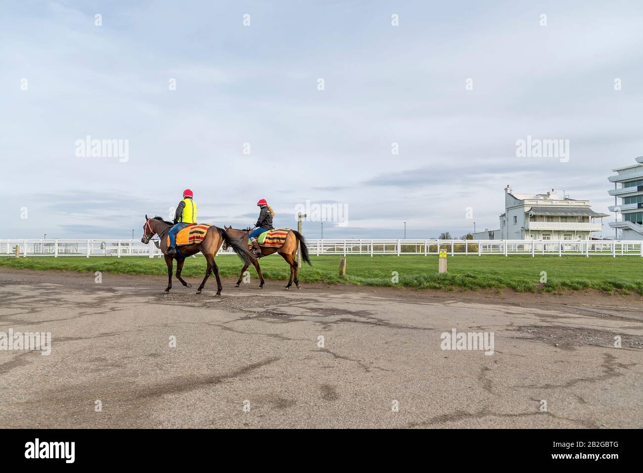 A male and female jockey exercise horses at Epsom Downs racecourse. The Princes Stand can be seen to the right of the photograph. Stock Photo