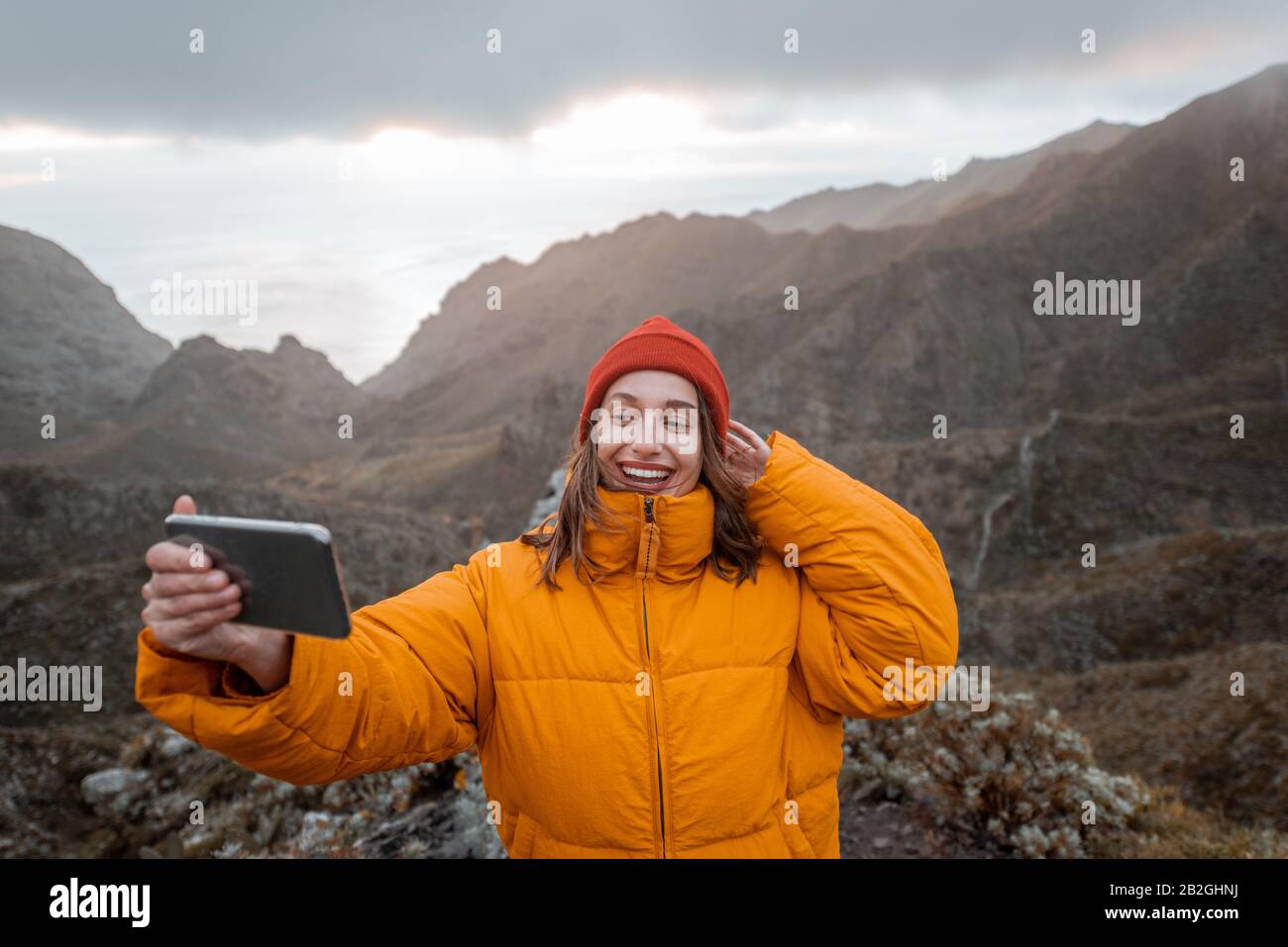 Portrait of a young traveler dressed in bright jacket and hat enjoying a trip highly in the mountains, traveling on Tenerife island, Spain Stock Photo