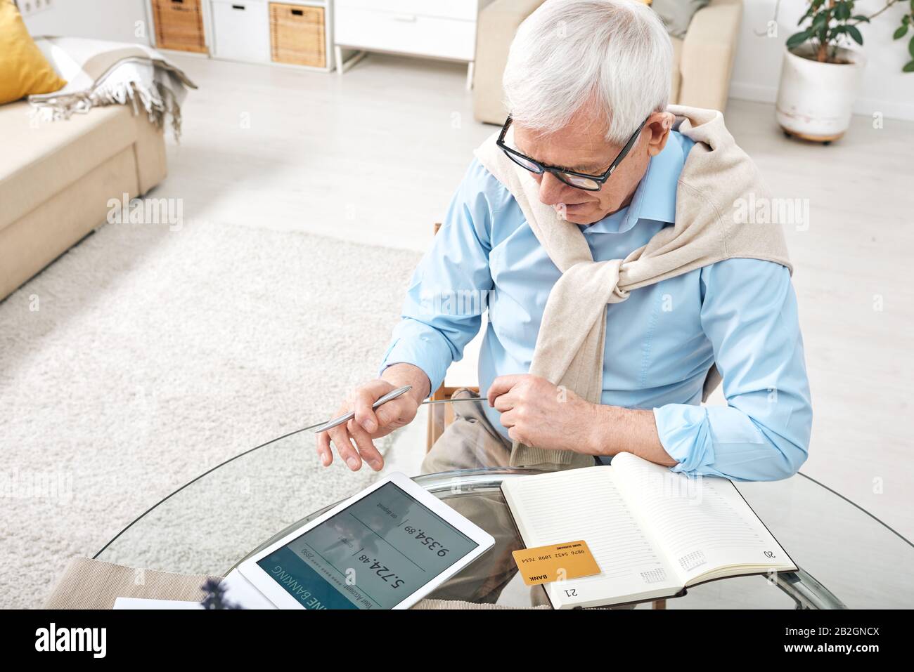 Content white-haired senior man sitting at glassy table and using tablet while analyzing own finances Stock Photo