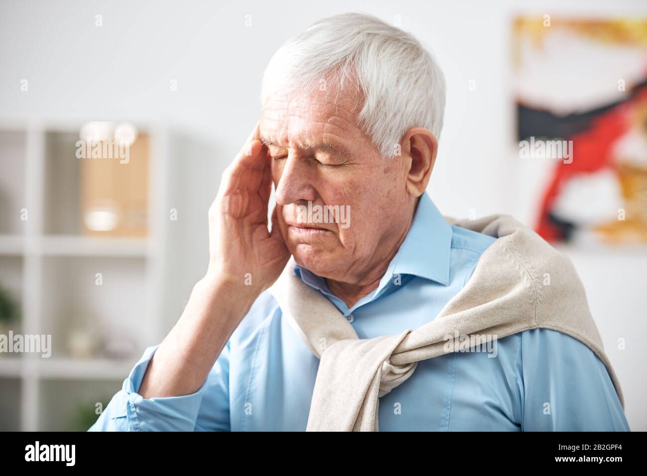 Exhausted senior white-haired man with closed eyes touching temple while feeling headache Stock Photo