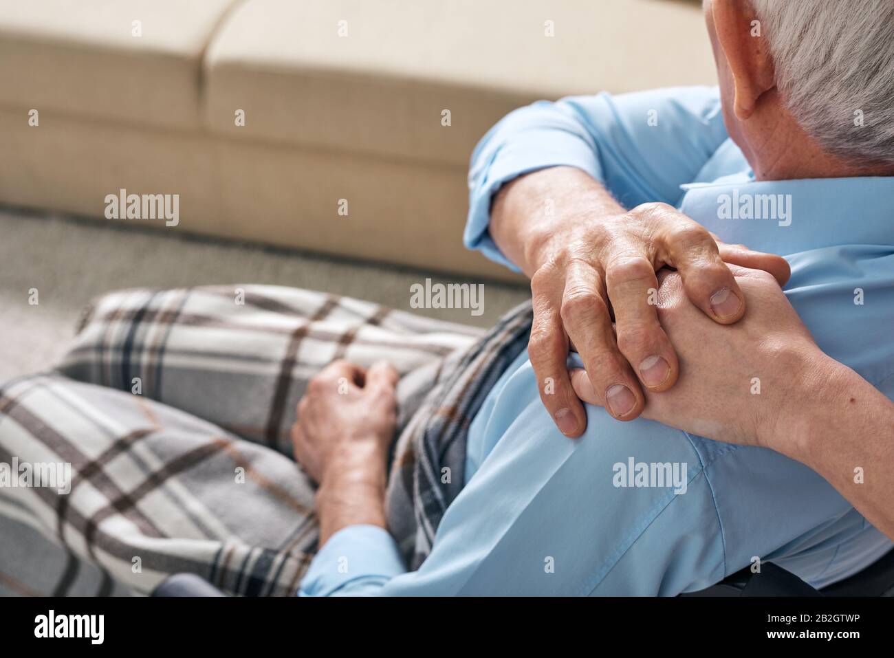 Over shoulder view of senior man with blanket on legs touching hand of