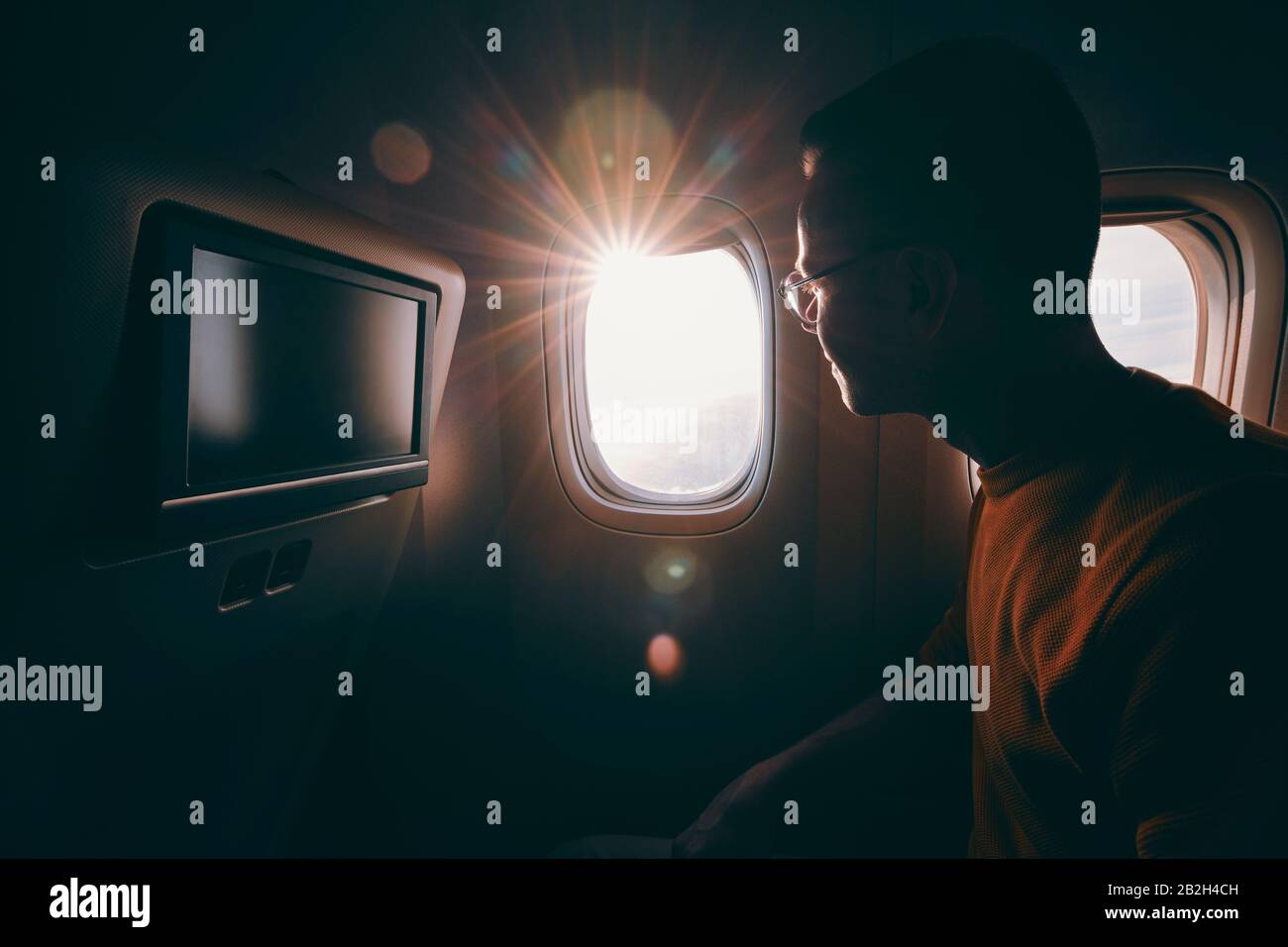 Travel by airplane during sunny day. Young man with eyeglasses looking through window. Stock Photo