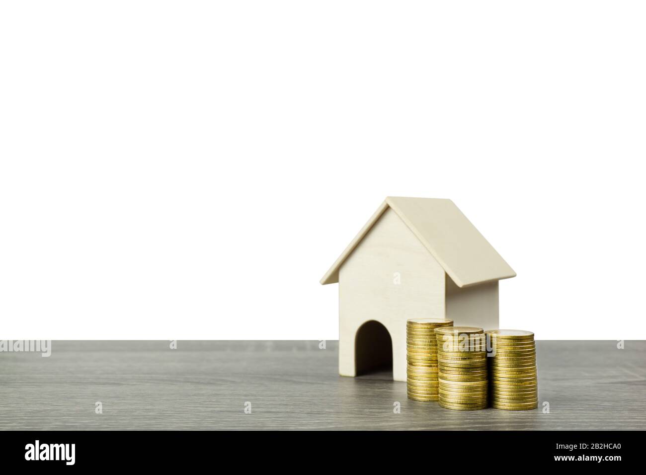 A small wooden house model with stack of golden coins on wood table isolated on white background. Stock Photo