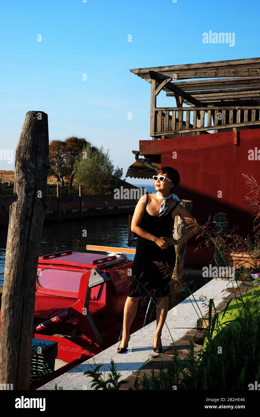 By a canal on the Venetian island of Mazzorbo La dolce vita, a retro styled film-star style fashion shoot with a little black dress Stock Photo