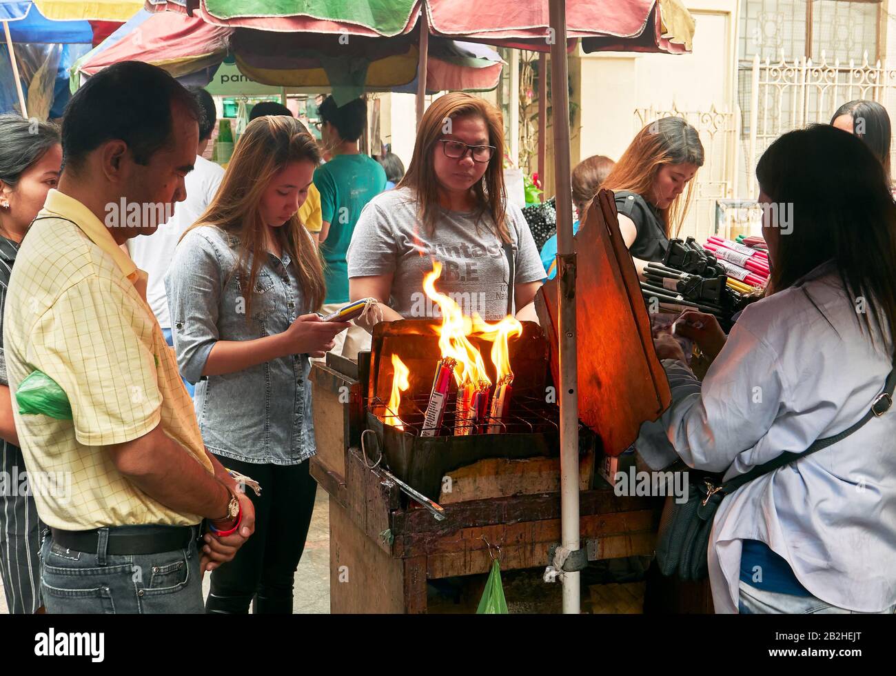 Manila, Philippines: Group of Filipinos praying and burning colourful candles at stalls around famous landmark Quiapo church Stock Photo