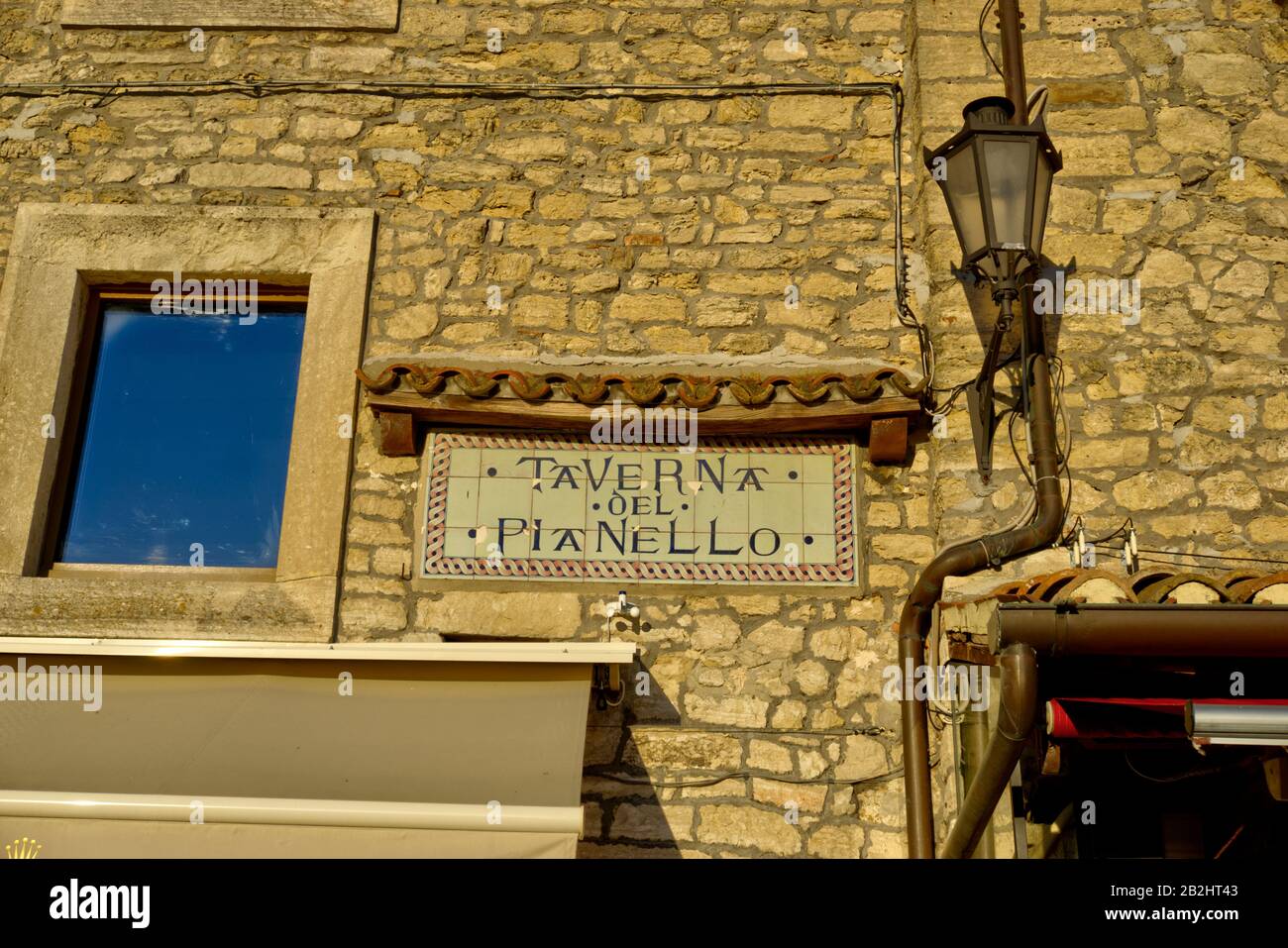 San Marino, San Marino - October 19, 2019: Sign on stone wall between lamp and window indicating restaurant called Taverna del Pianello. Stock Photo