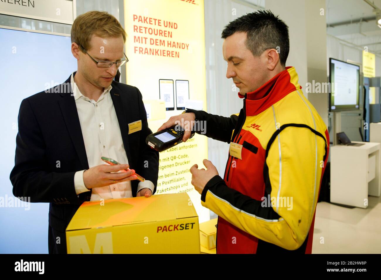 03 March 2020, Berlin: David Krakow (l), Product Manager at DHL Post &  Paket Deutschland, demonstrates how to frank parcels with a mobile phone.  In a press conference, the company presented its