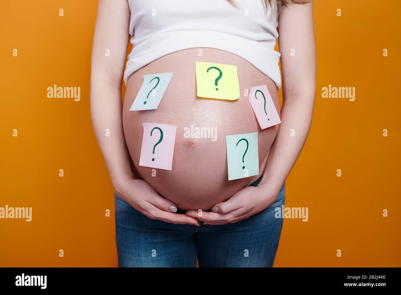 Pregnant woman with question marks on paper stickers on tummy on yellow background Stock Photo