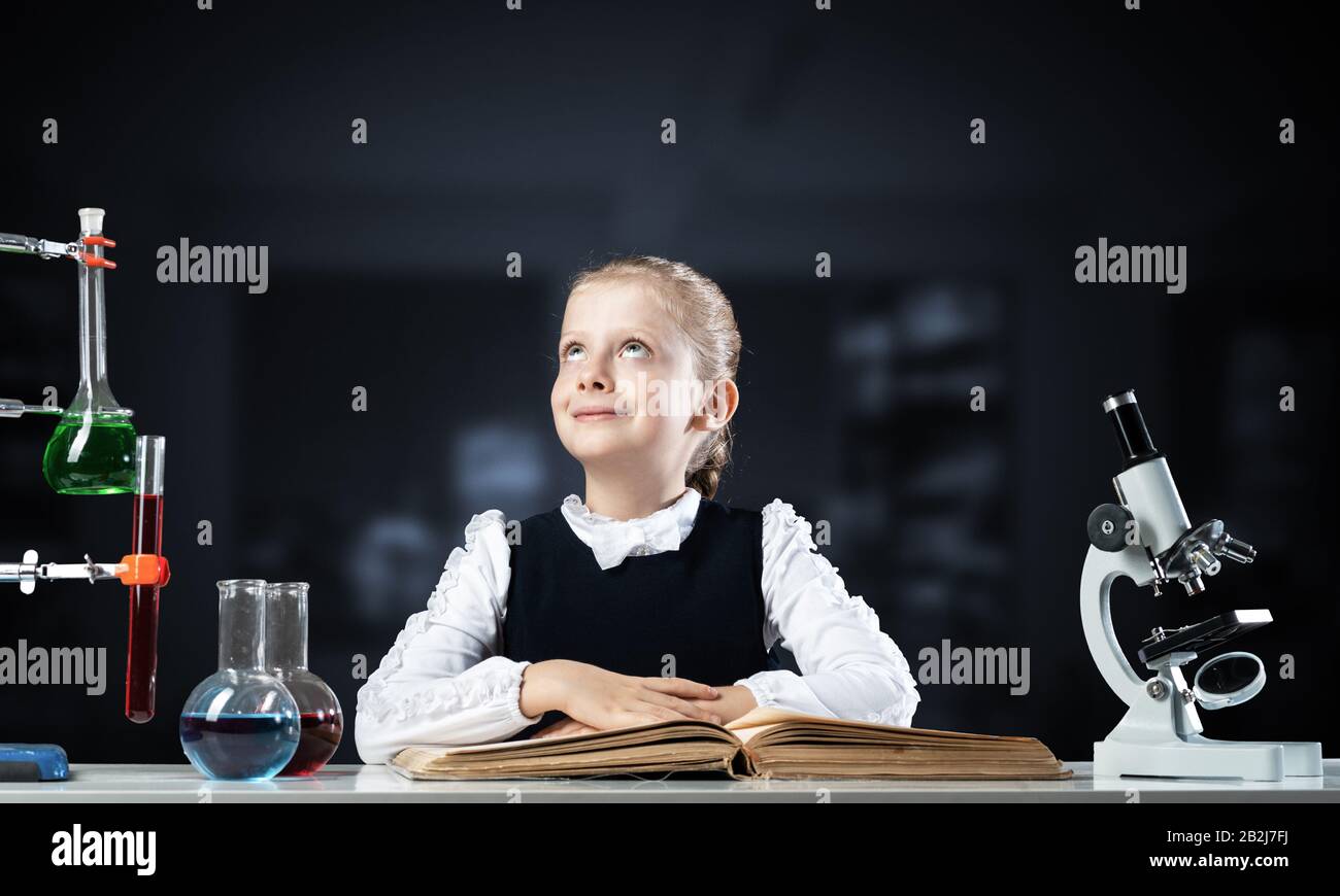 Smiling little girl sitting at desk with open book Stock Photo - Alamy