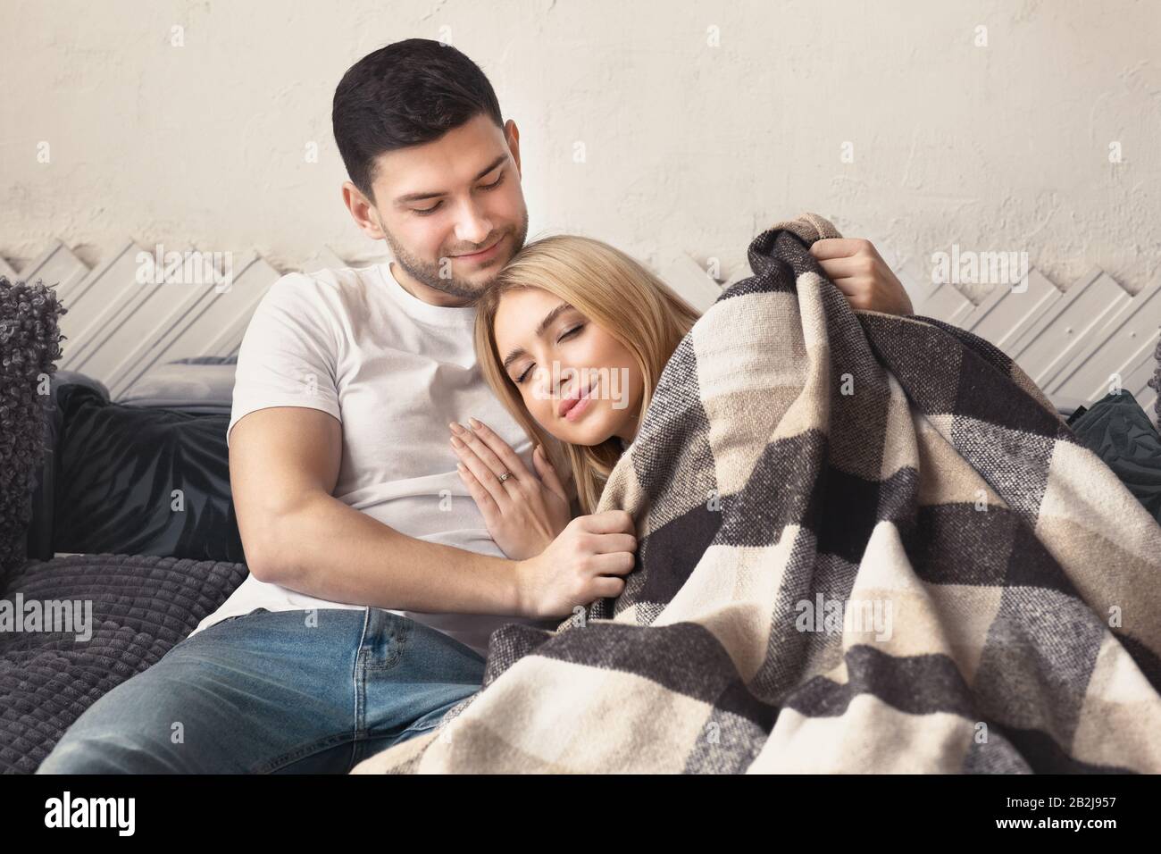Affectionate young couple with warm plaid resting at home Stock Photo