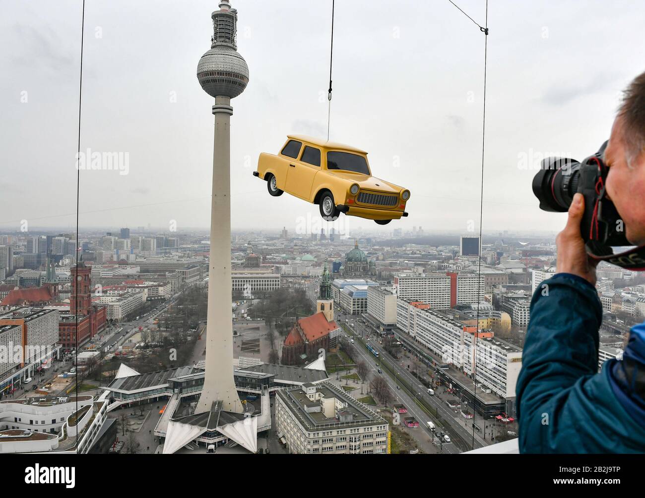 Berlin, Germany. 03rd Mar, 2020. A replica Trabant hangs at the Park Inn  Hotel at the Base Flying facility above Alexanderplatz with a view over the  city centre of Berlin. The Little