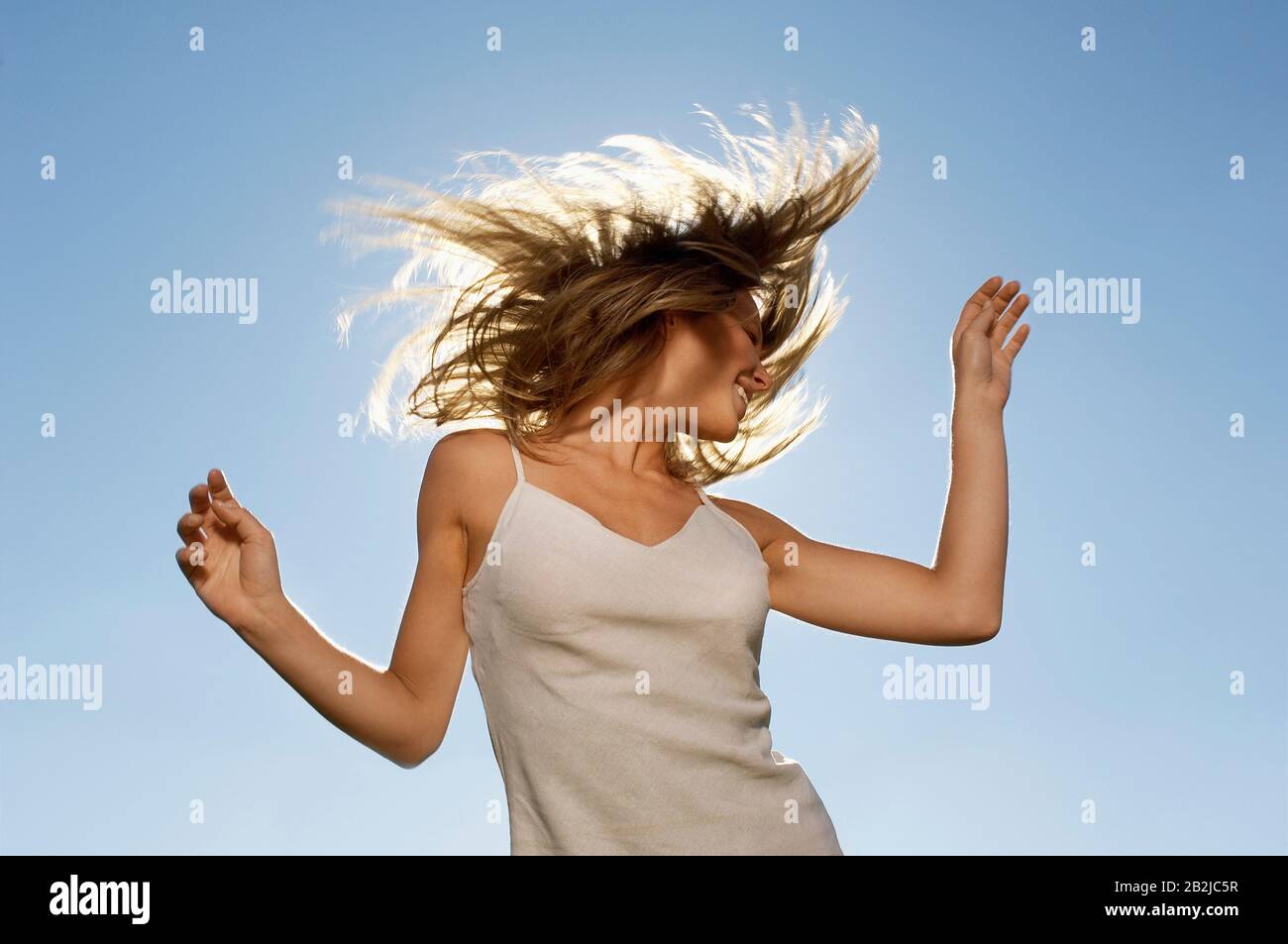 Young woman standing in front of sun tossing hair low angle view Stock Photo