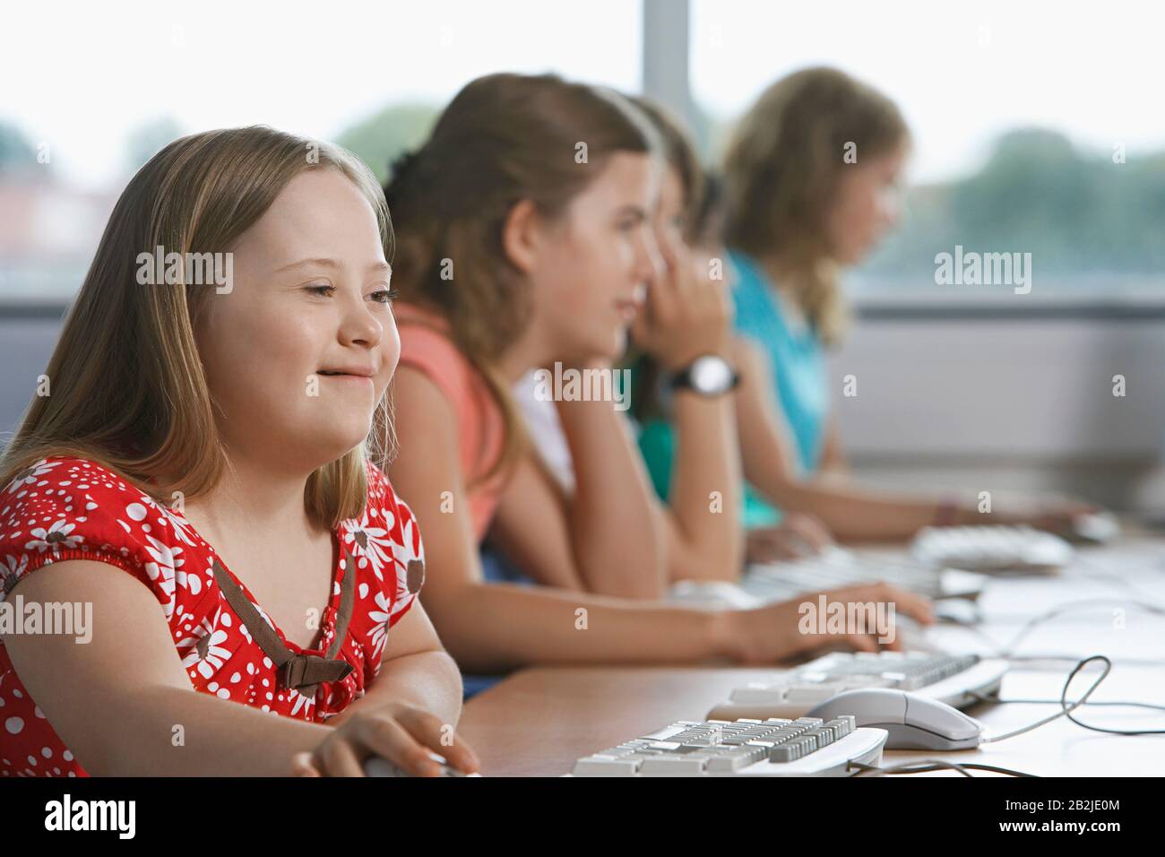 Girl (10-12) with Down syndrome using computer in computer lab children in background Stock Photo