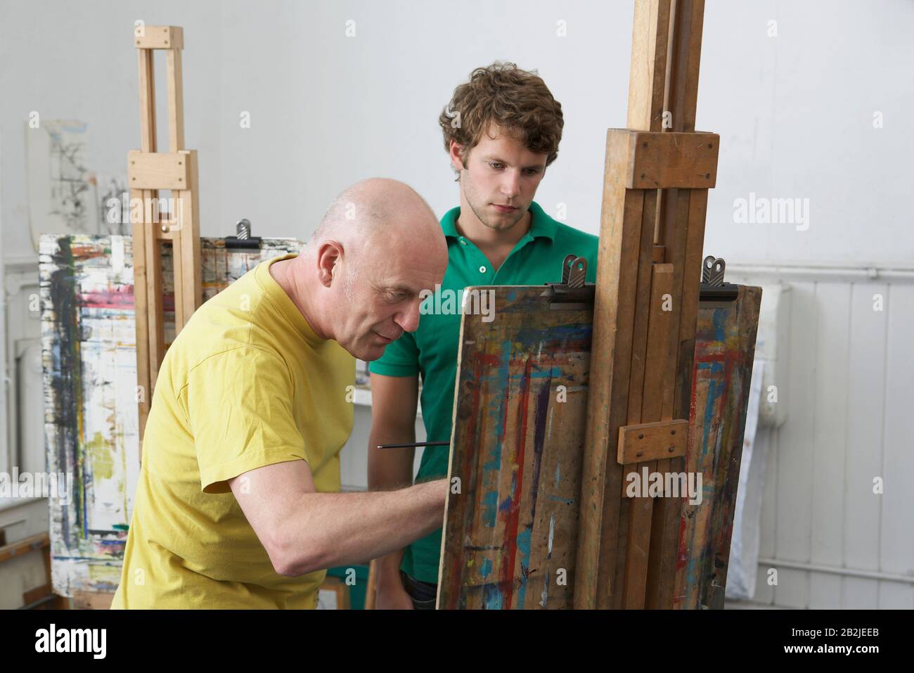 Student looking on as artist paints at easel in art studio Stock Photo