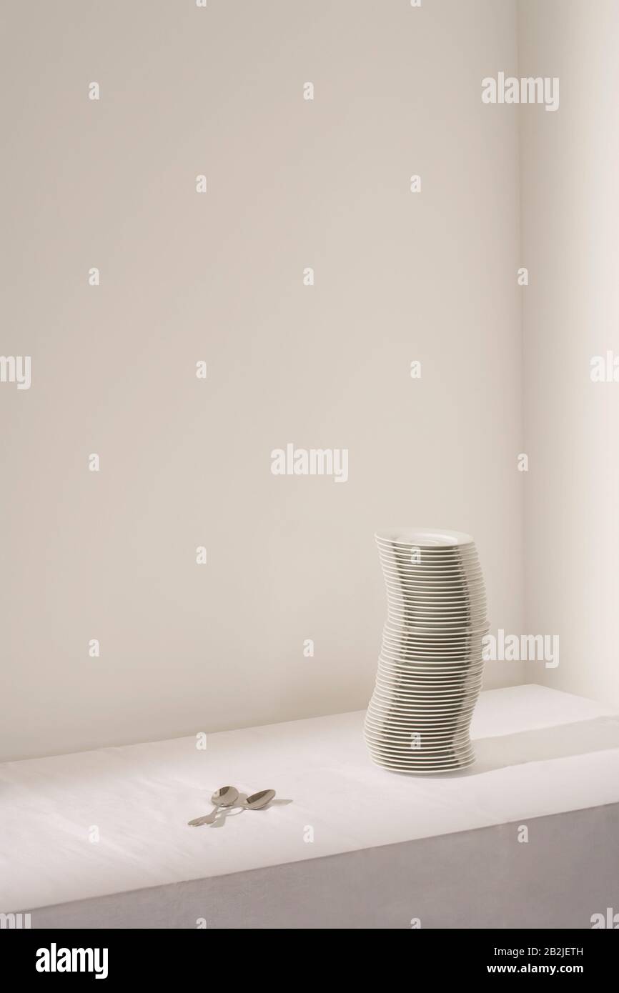 Spoons next to stack of plates on table Stock Photo