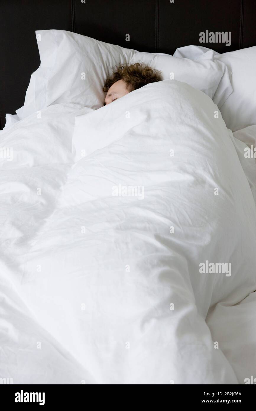 Man sleeping in bed covered under duvet elevated view Stock Photo Alamy