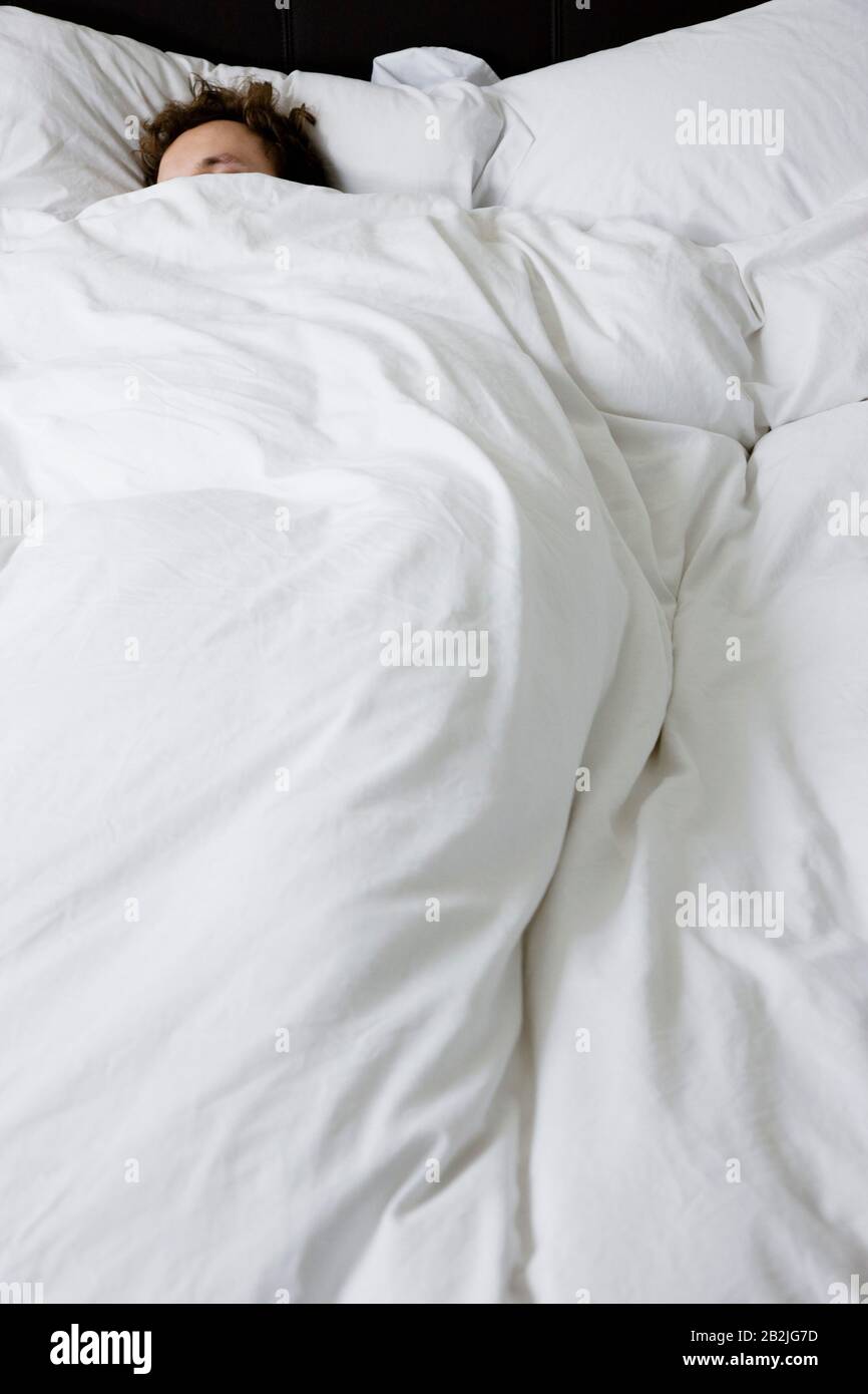 Man sleeping in bed covered under duvet elevated view Stock Photo Alamy