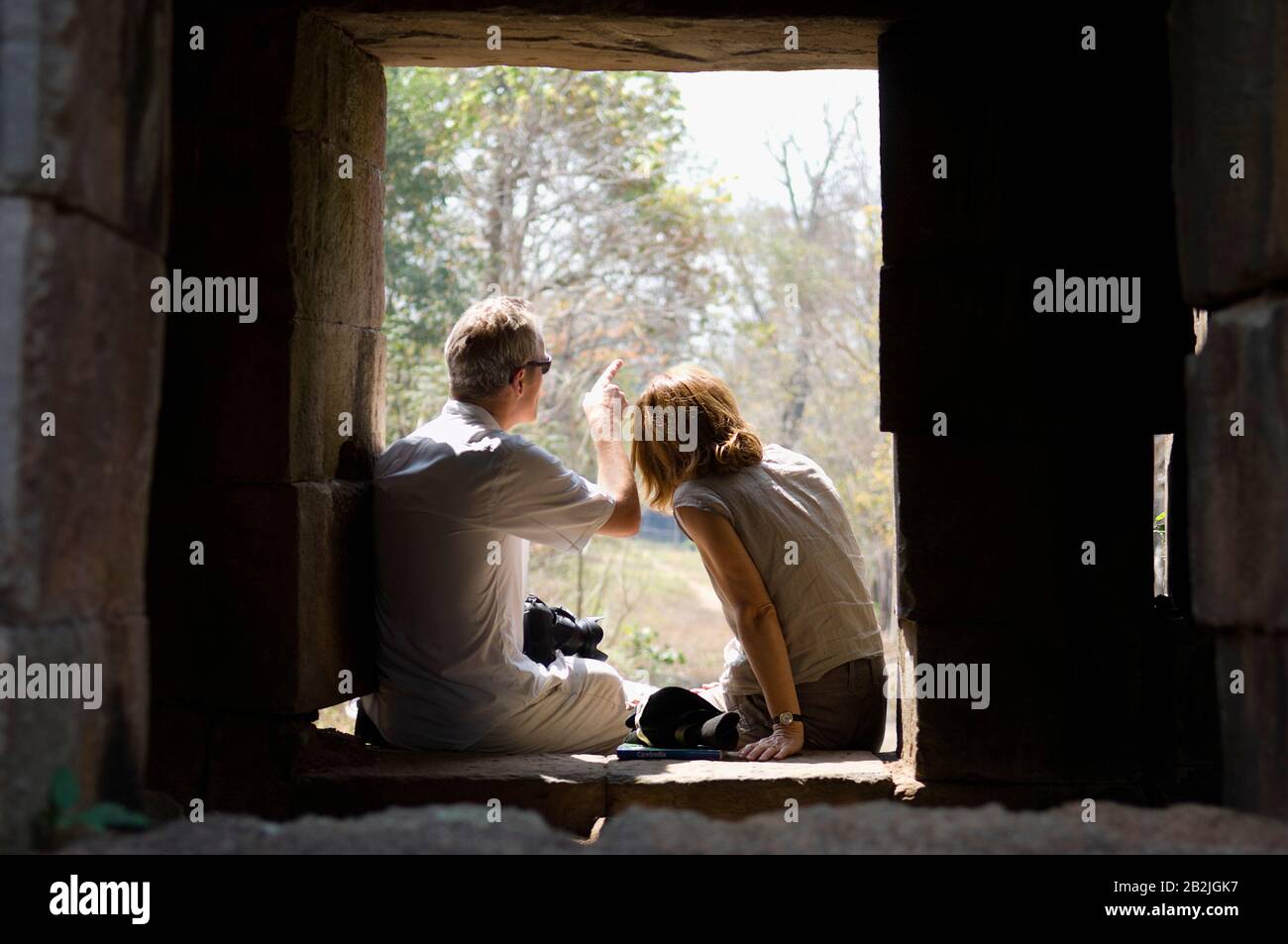 Couple Sitting in Window of Stone Building Stock Photo