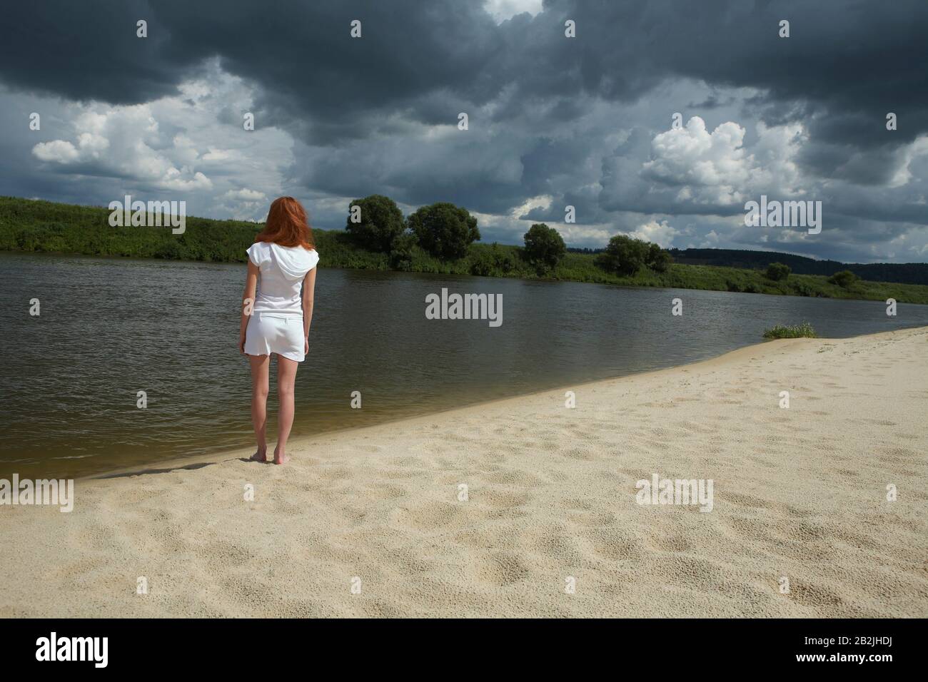 Woman Standing by River under Storm Clouds Stock Photo