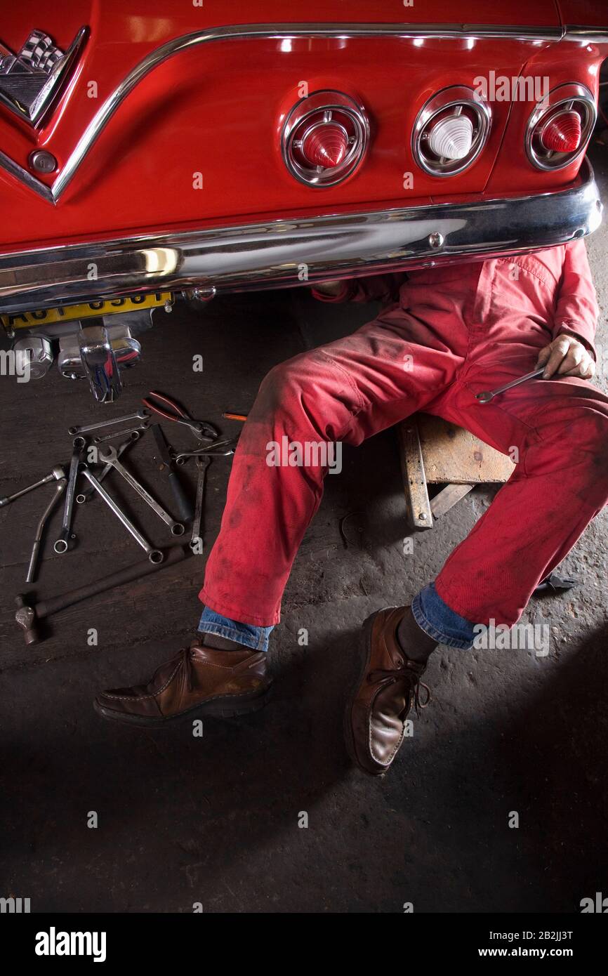 Mechanic working Under Back of Vintage Car Stock Photo