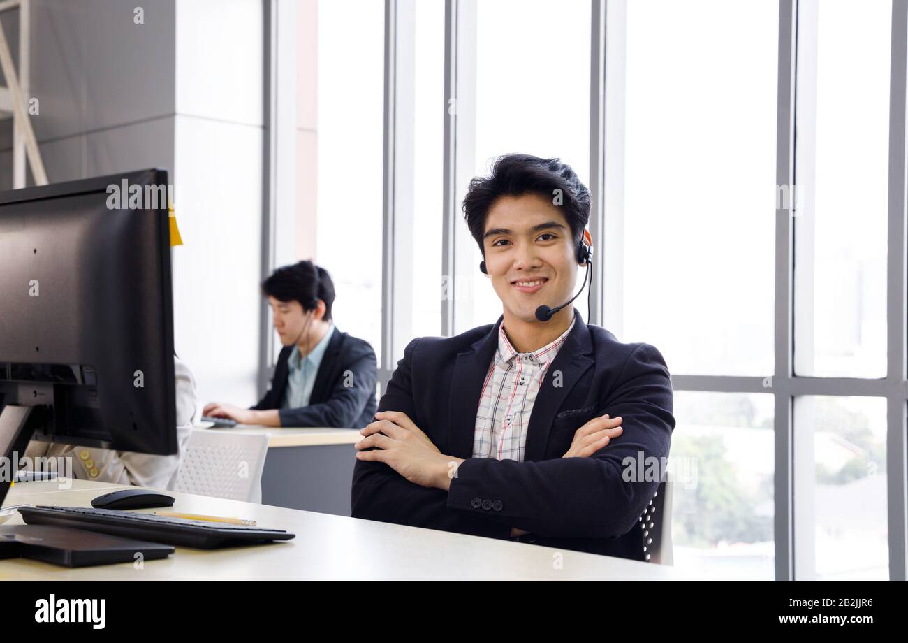 Smiling confident Asian male call center operator enjoy his work at office. Concept for customer support service, lifestyle at office, employee. Stock Photo