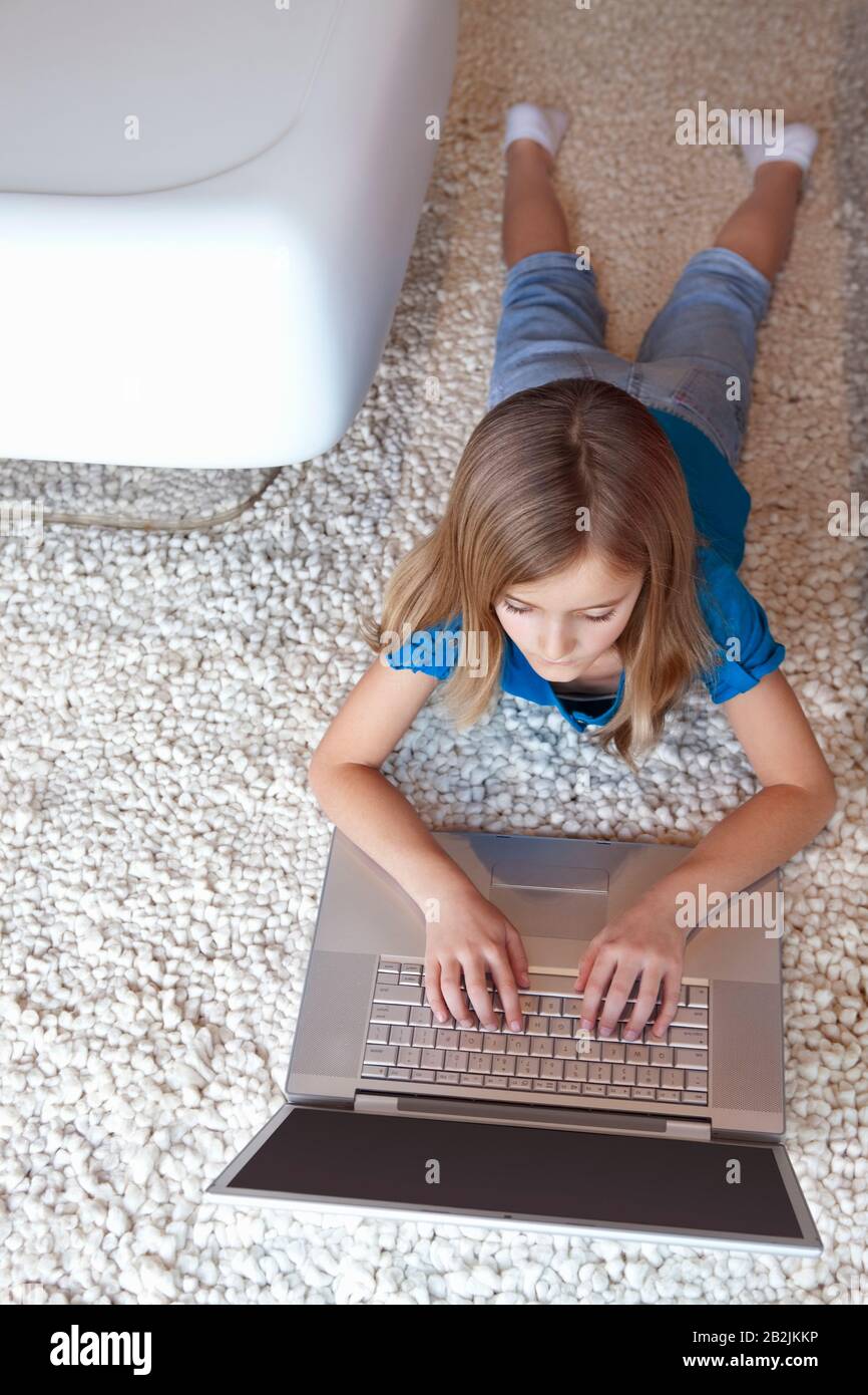 Young girl with laptop lying on rug Stock Photo - Alamy