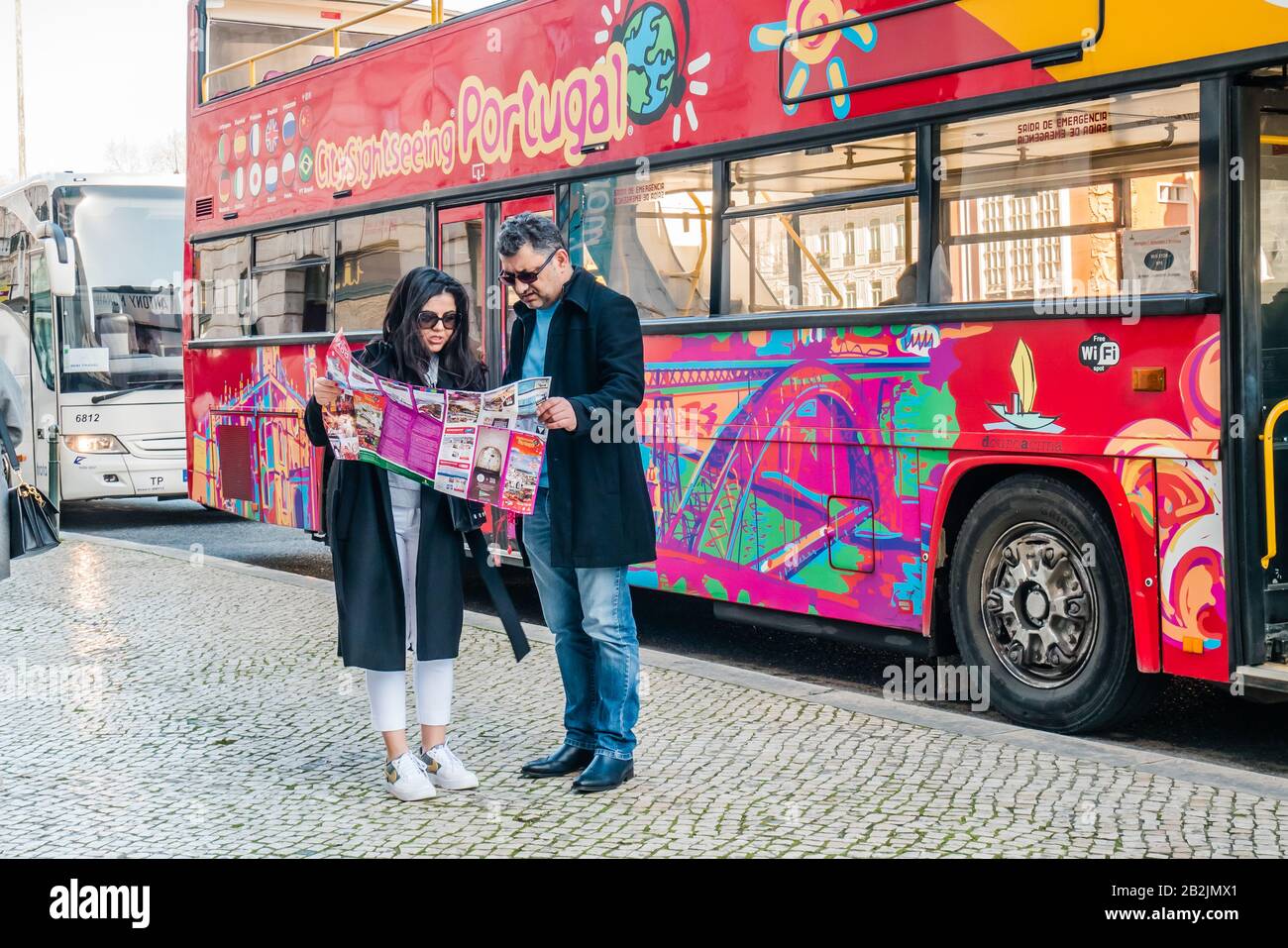 A traveling couple checking map for direction in front of a city sight seeing bus in Lisbon Portugal Europe Stock Photo