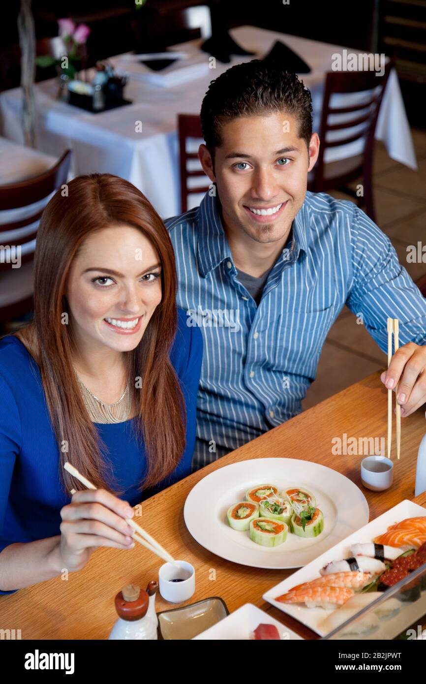 Portrait of a happy couple eating sushi with chopsticks in Japanese restaurant Stock Photo