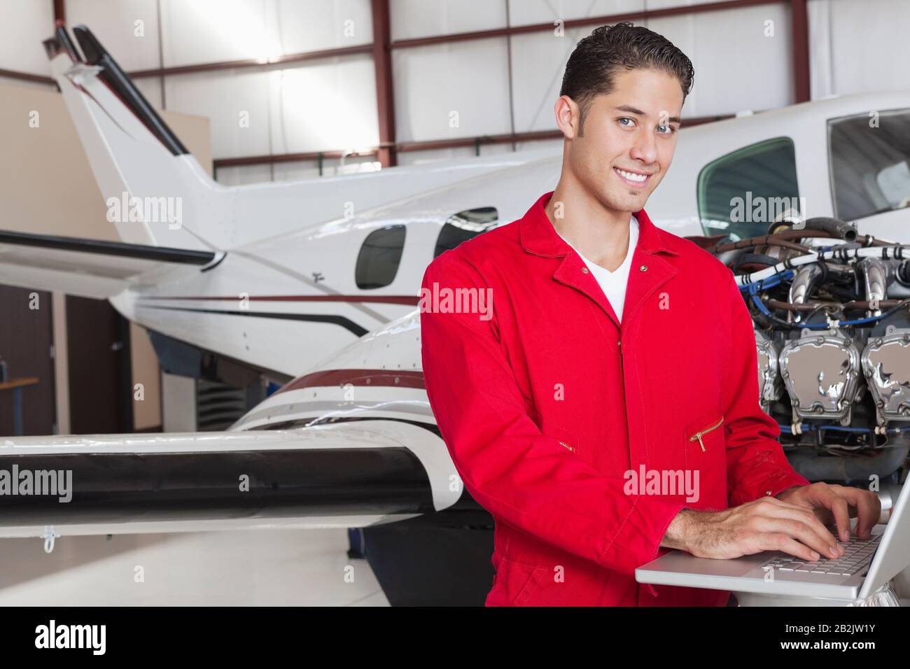 Portrait of young aeronautic engineer using laptop in front of airplane Stock Photo