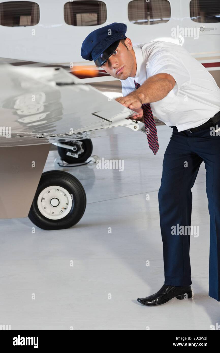 Portrait of happy young male pilot inspecting airplane's wing Stock Photo