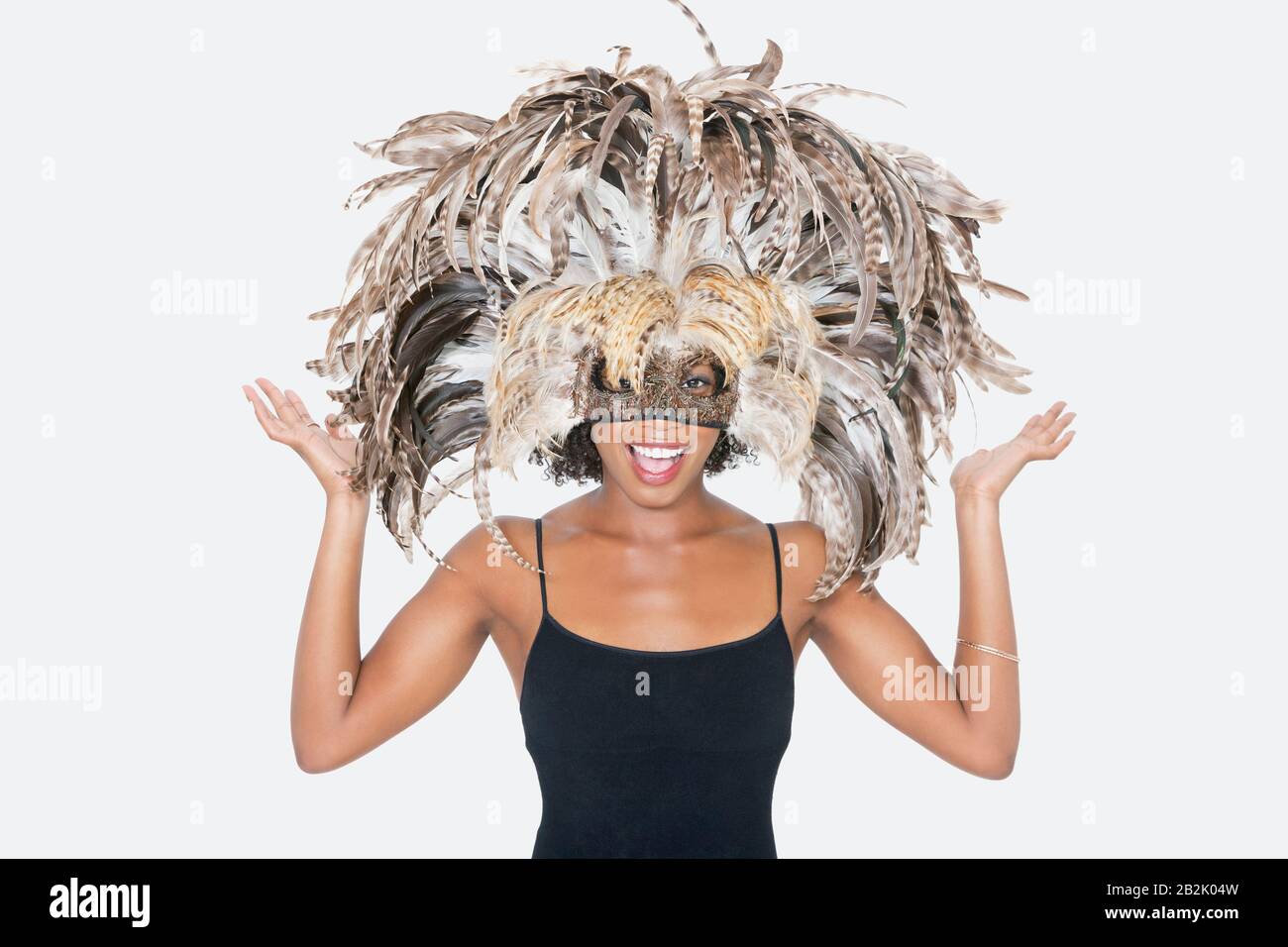 Portrait of happy African American woman wearing a feather mask over gray background Stock Photo