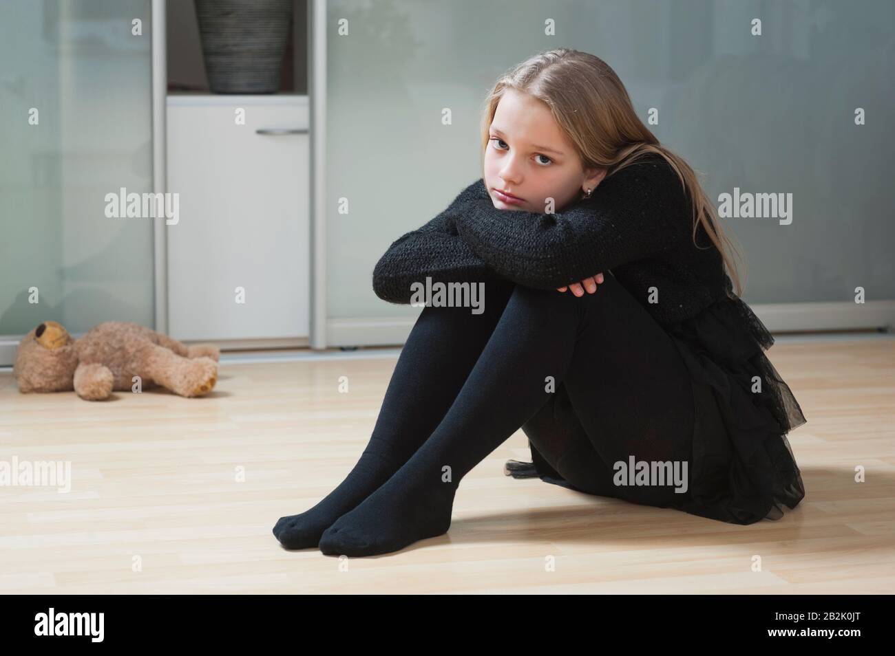 Portrait of an upset girl sitting on hardwood floor Stock Photo - Alamy