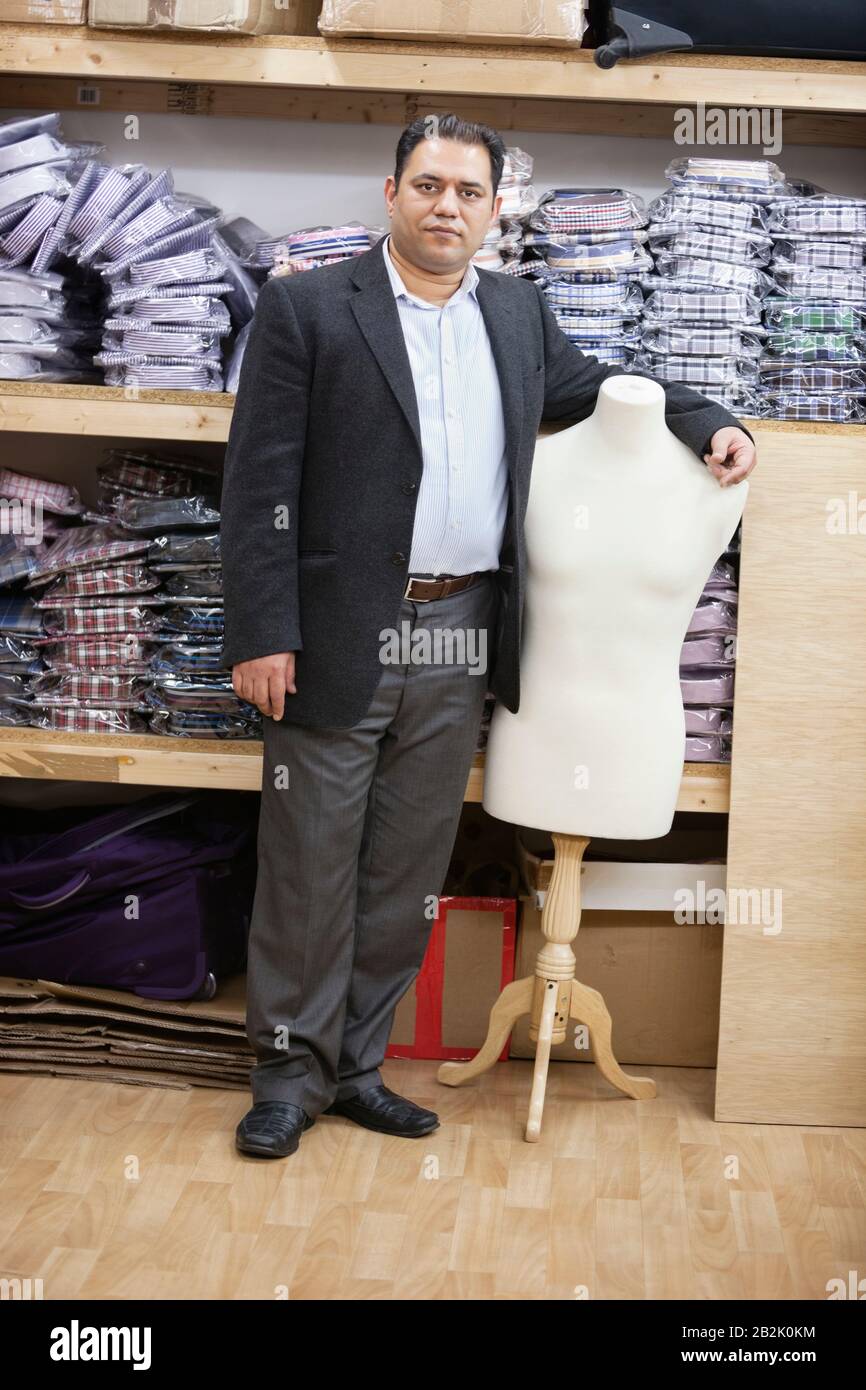 Portrait of male owner standing by tailor's dummy in clothing store Stock Photo