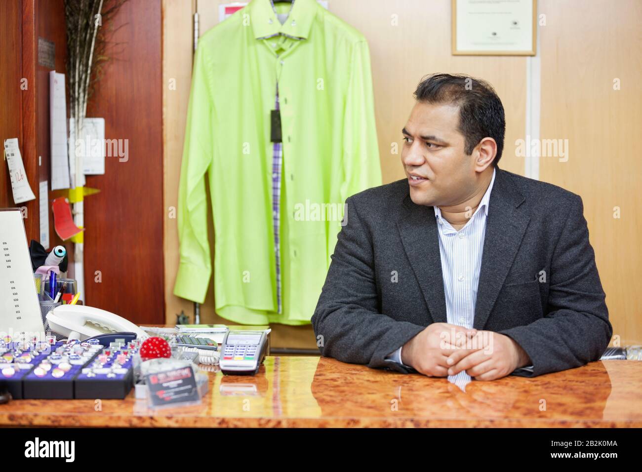 Mid adult male salesperson sitting at desk in menswear store Stock Photo