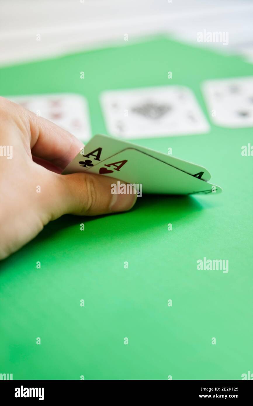 Cropped shot of hand holding aces of hearts and clubs on green surface Stock Photo