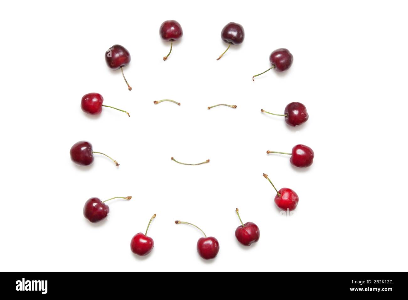 Cherries surrounding smiley face made by stems on white background Stock Photo
