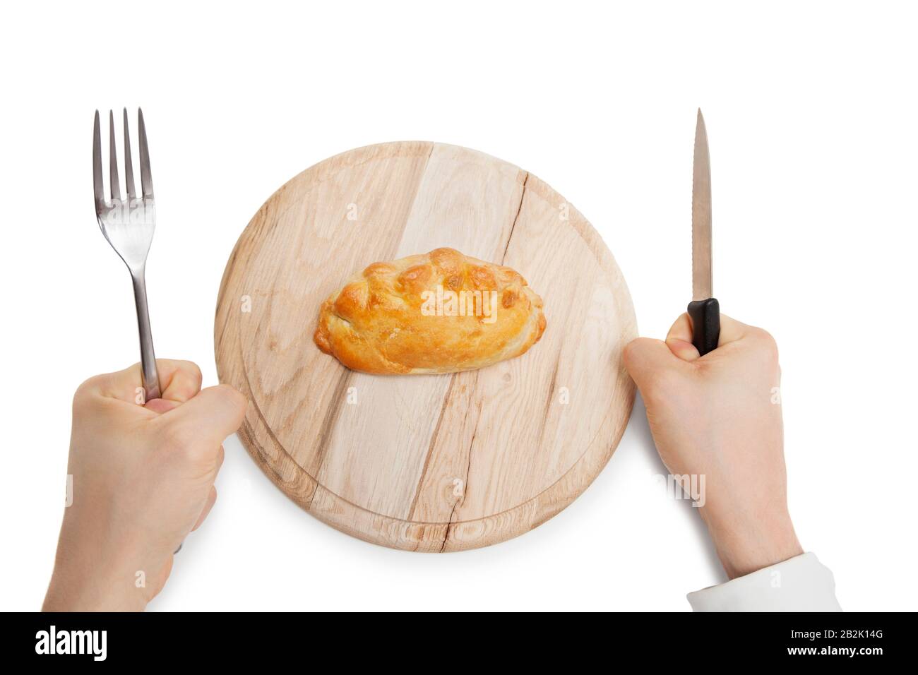 Hands holding knife and fork with Cornish pastry on wooden plate over white background Stock Photo
