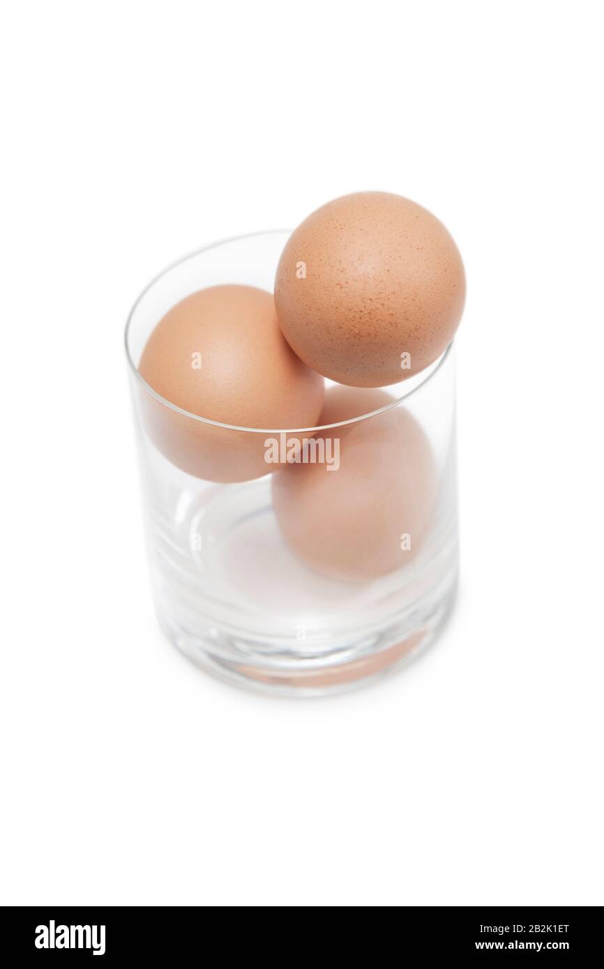 Three brown eggs in drinking glass over white background Stock Photo