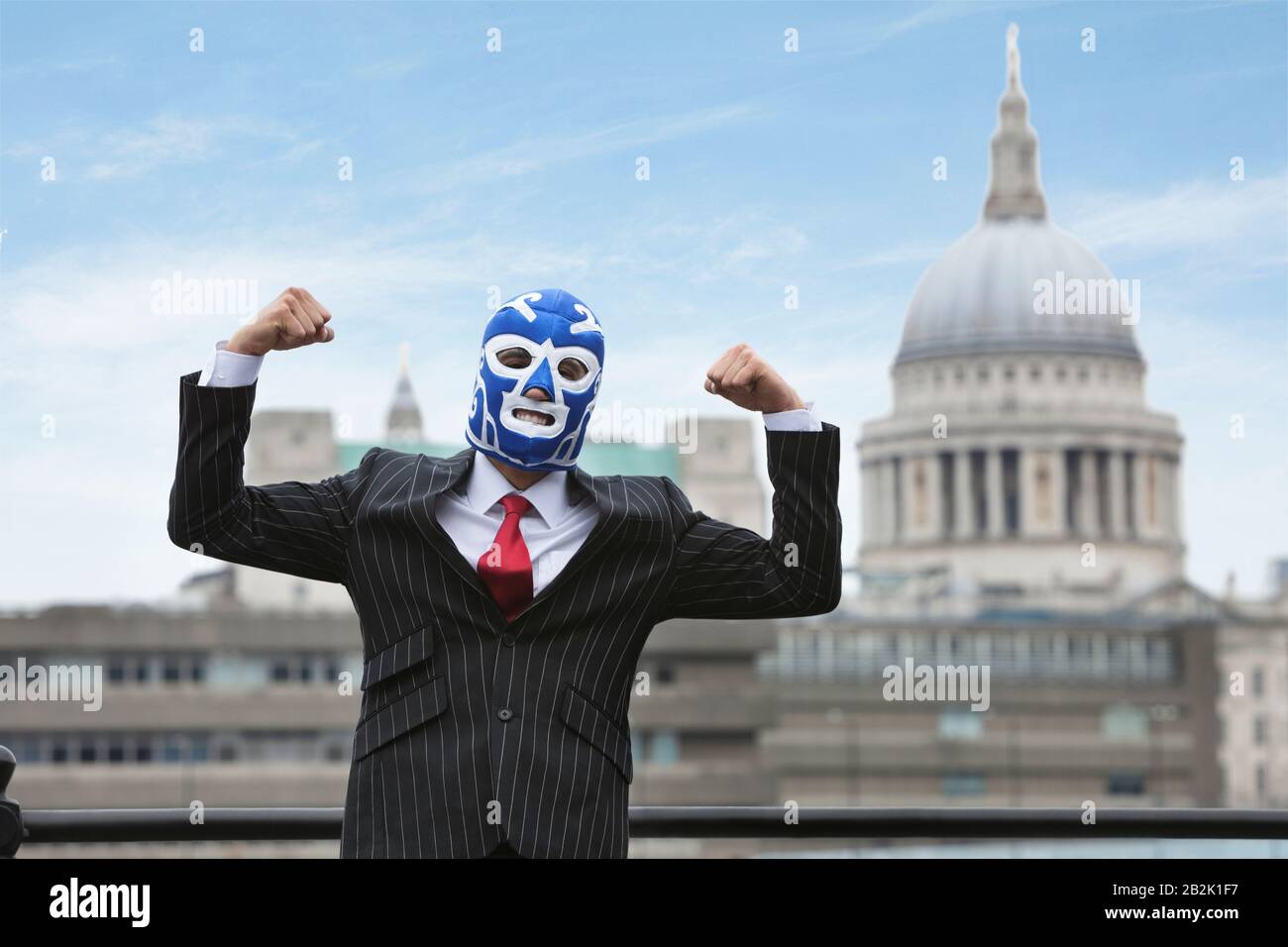 Young businessman flexing muscles while wearing wrestling mask with St. Paul's Cathedral building in the background Stock Photo