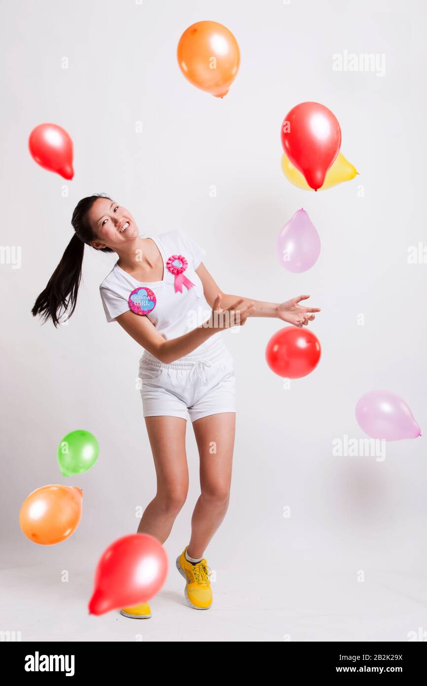 Portrait of playful young woman with multicolored balloons celebrating her birthday against white background Stock Photo