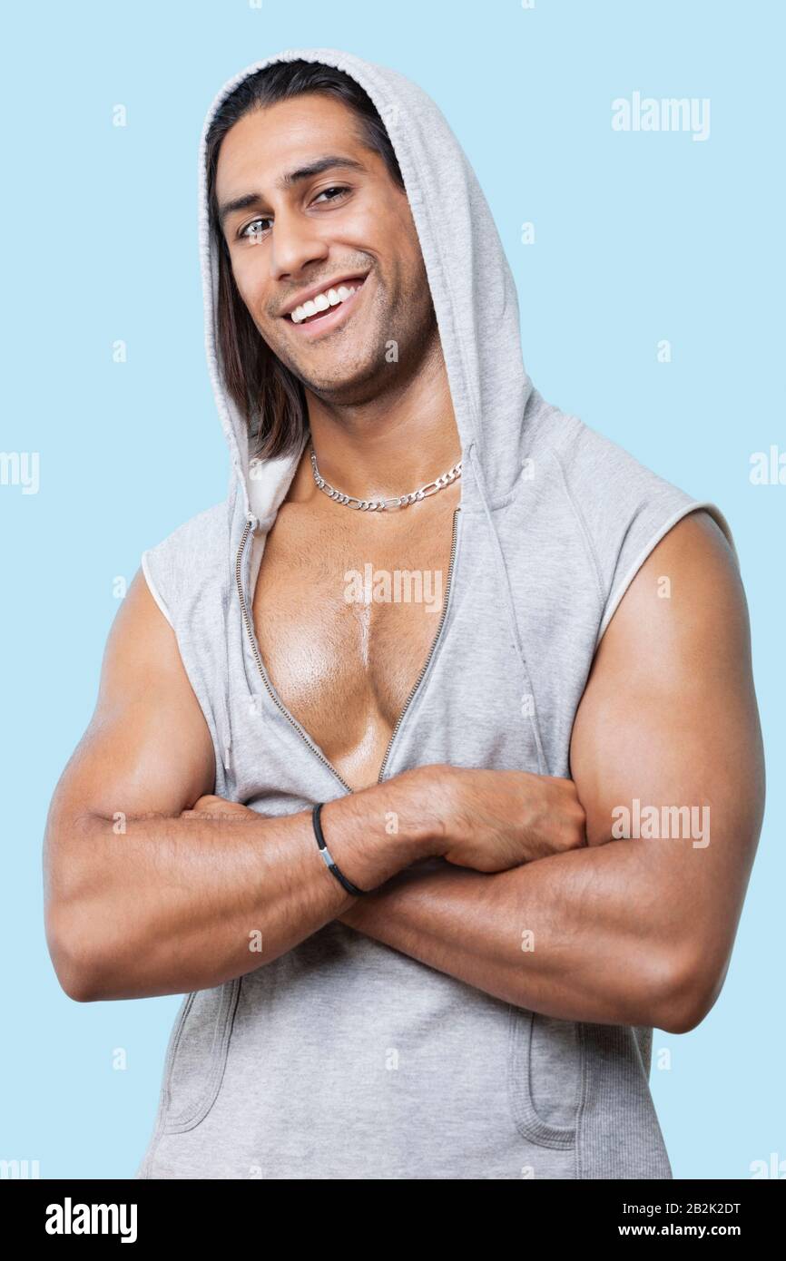 Portrait of happy young muscular man wearing hooded jacket standing against colored background Stock Photo