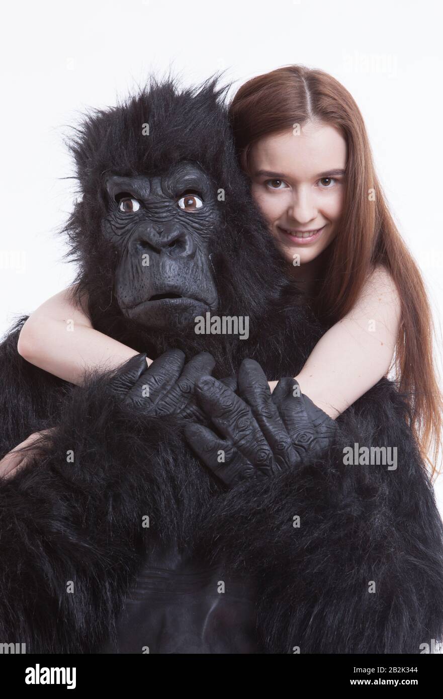 Portrait of smiling young woman hugging man in gorilla costume against white background Stock Photo