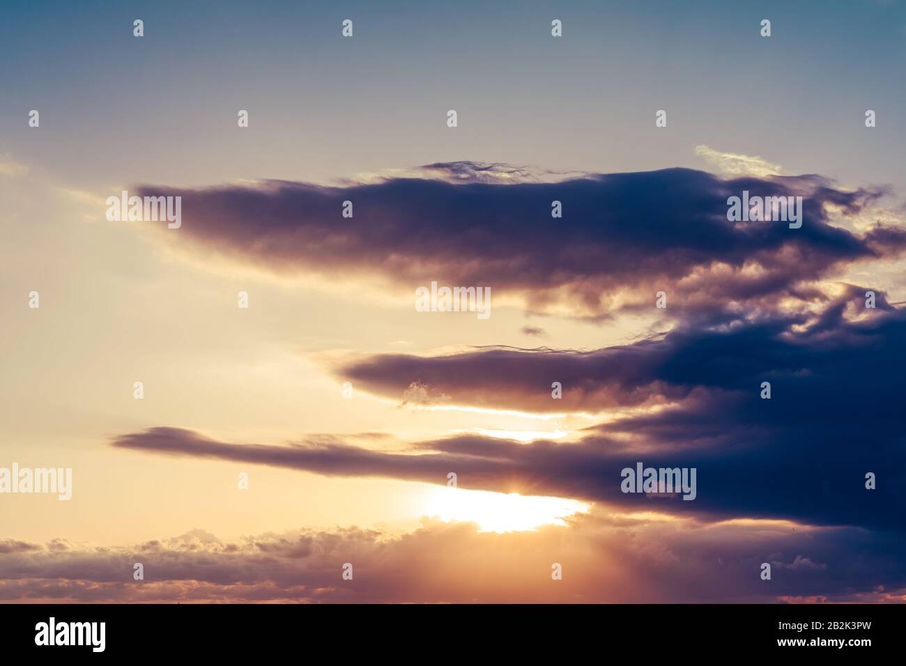 Sunrise, the sun is shining strong from the horizon over all the clouds and under the blue sky Stock Photo