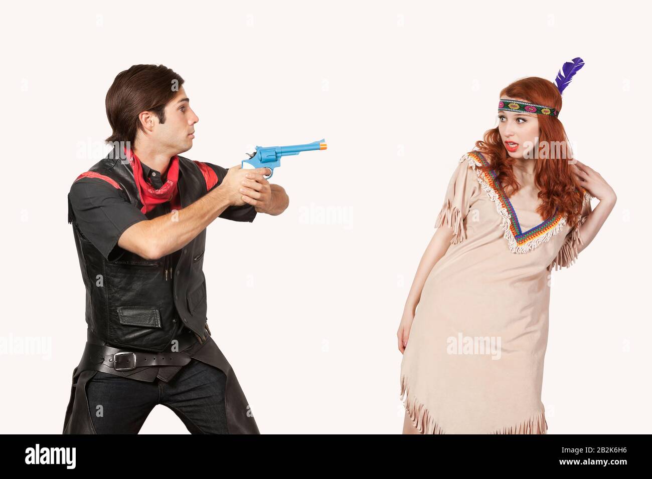 Young cowboy aiming gun at woman in old-fashioned costume against gray background Stock Photo